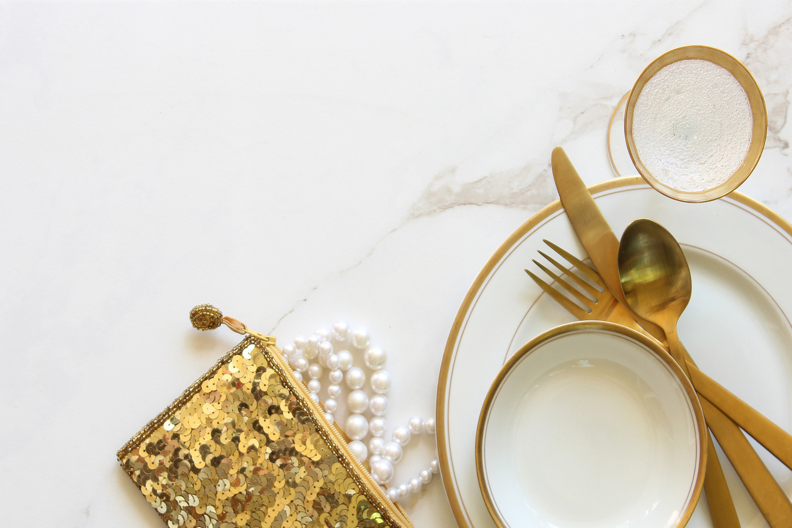 Elegant white and gold table setting with gold sequined purse and pearls. White marble copy space.