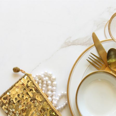 Elegant white and gold table setting with gold sequined purse and pearls. White marble copy space.